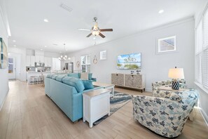 A spacious living area with a sectional sofa, a patterned armchair, a dining table, and a kitchen in the background. - Sandy Cheeks | Pet-Friendly + Pool + Putting Green (Orange Beach)