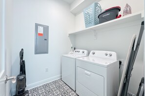 Ein Waschraum mit zwei weißen Whirlpool-Waschmaschinen, einem Staubsauger von Shark und einem Stromzähler an der Wand.