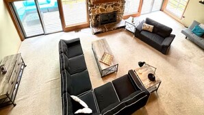 A spacious loft-style room with a stone fireplace, large windows, and a ceiling fan. - Private 13-Acre Retreat - Pond, Kayaks, Fire Pit & Trails. Pet-friendly! (Conneautville)