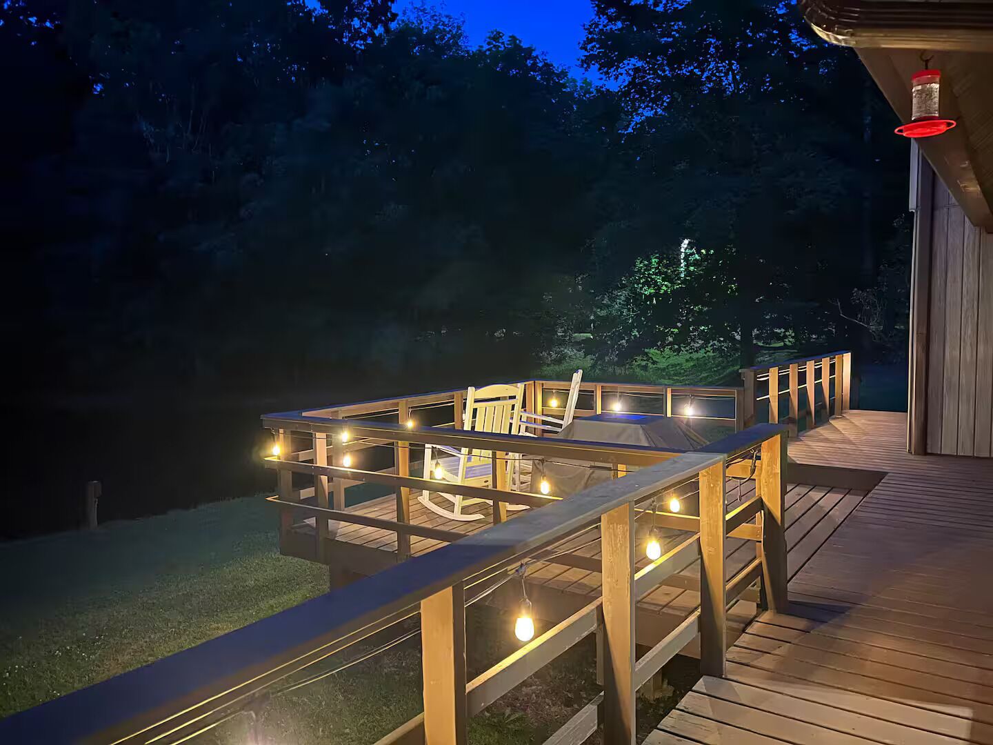 Une terrasse en bois avec une enceinte en verre, des guirlandes lumineuses et une chaise.