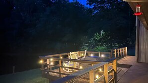 A wooden deck with a glass enclosure, string lights, and a chair. - Private 13-Acre Retreat - Pond, Kayaks, Fire Pit & Trails. Pet-friendly! (Conneautville)