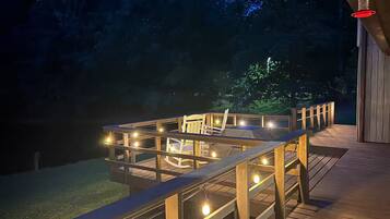 Une terrasse en bois avec une enceinte en verre, des guirlandes lumineuses et une chaise.
