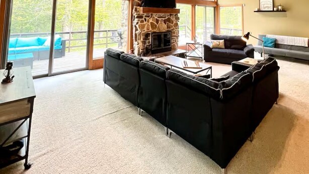 A spacious living area with a stone fireplace, large windows, and a high wooden ceiling. - Private 13-Acre Retreat - Pond, Kayaks, Fire Pit & Trails. Pet-friendly! (Conneautville)