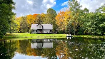 Un chalet au bord du lac, doté d’un quai, entouré d’un feuillage automnal et surplombant un ciel dégagé.