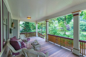 Eine überdachte Veranda mit Korbmöbeln, einem Holzwertlauf und Blick auf einen üppigen Garten.