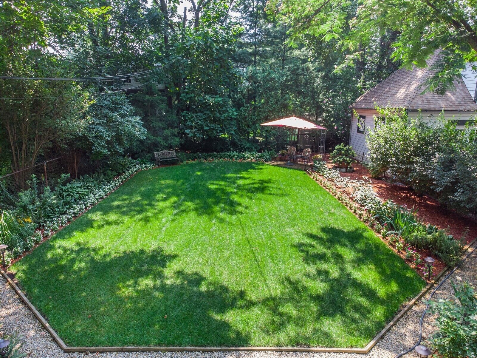 A well-maintained backyard with a lawn, garden beds, and a patio area.
