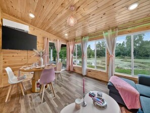 A wooden interior with a dining area, a sofa, and large windows.
