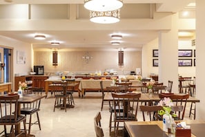 Un comedor de hotel con mesas y sillas de madera, una cocina al fondo y un candelabro.