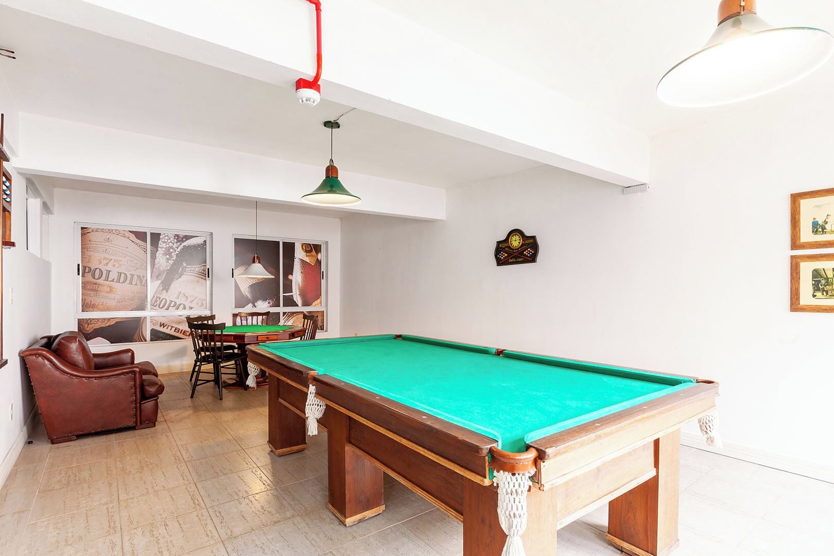 Een biljart tafel in een ruimte met een hoge plafond, een eettafel met stoelen, en een hangende lamp.