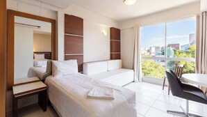 Camera d'albergo con un letto, una scrivania, una sedia, un'ampia finestra con vista sulla città e una lampada a parete.
