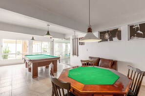 Una habitación amplia con mesa de billar, mesa de futbolín y una mesa cubierta de fieltro verde.