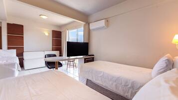 A hotel room with two beds, a desk, a chair, a TV, and an air conditioning unit.