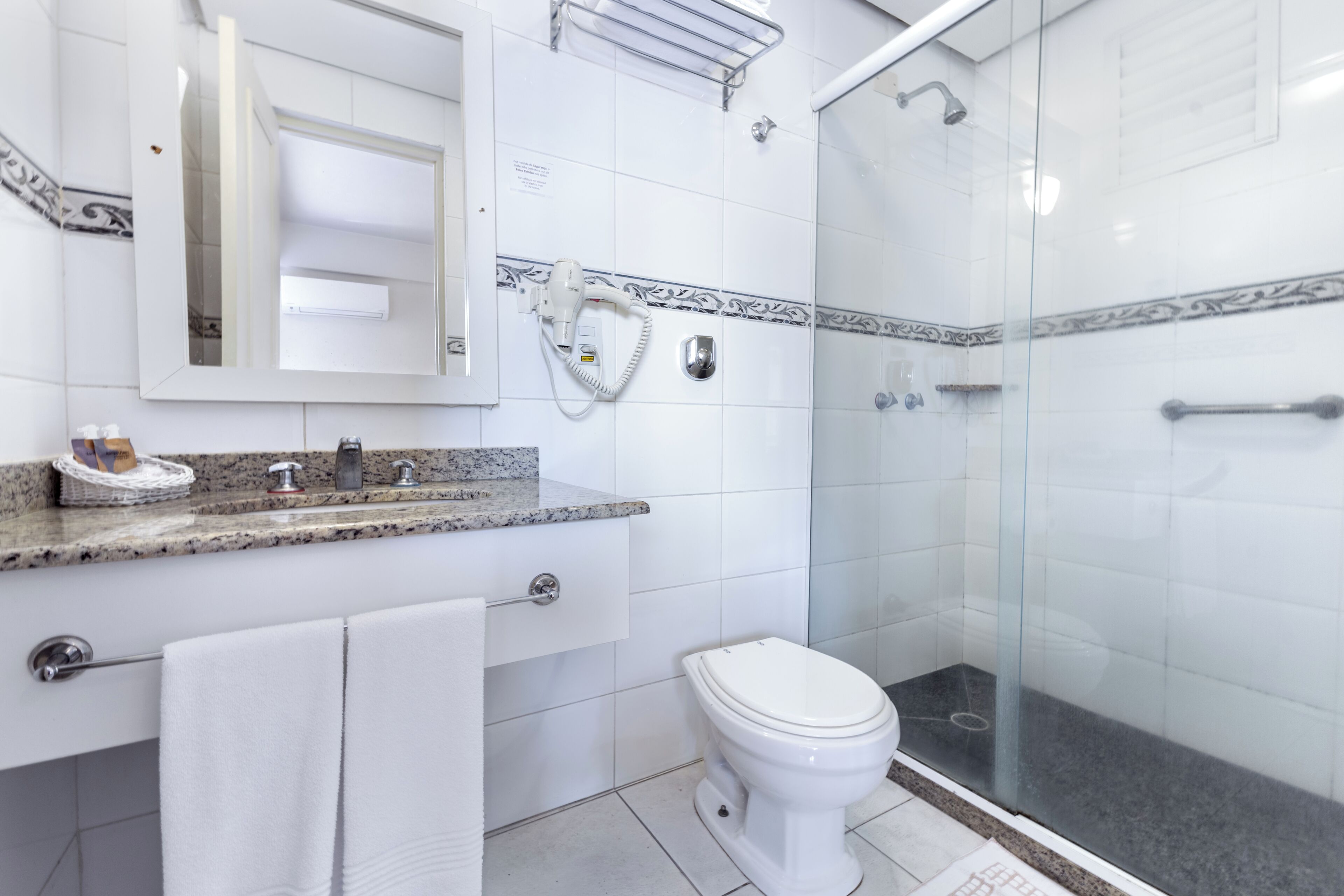 A bathroom with a toilet, a sink, a mirror, a towel rack, and a shower enclosure.