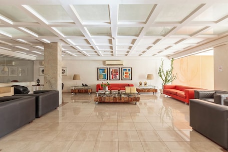 A spacious living area with a high ceiling, a central coffee table, and multiple seating options including sofas and armchairs.. TRI HOTEL EXECUTIVE SANTA MARIA