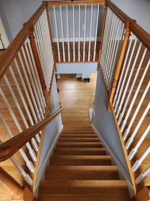 Eine Holztreppe mit weißen Geländern führt zu einer Plattform, wo Schuhe stehen.