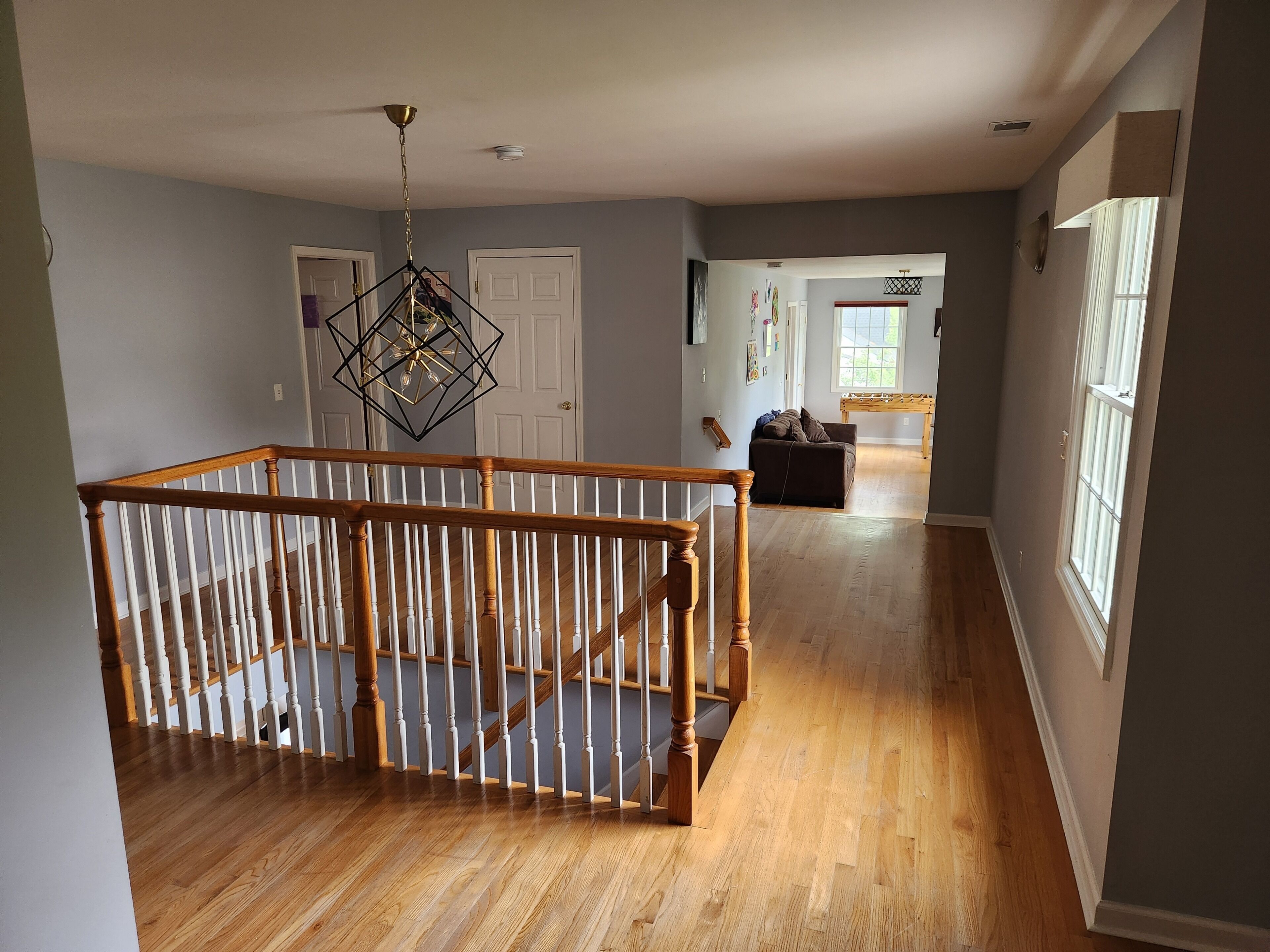 A spacious room with a wooden staircase, a hanging light fixture, and a view into another room with a couch.