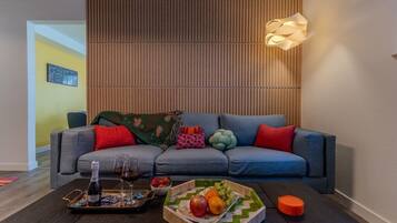 A modern living room with a grey sofa, colorful cushions, a wooden slatted wall, and a unique pendant light.