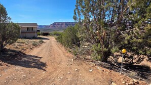 Uma estrada de terra que leva a uma casa, com montanhas ao fundo.