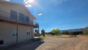 Um edifício de dois andares com varanda, entrada por caminho de pedras e céu claro.