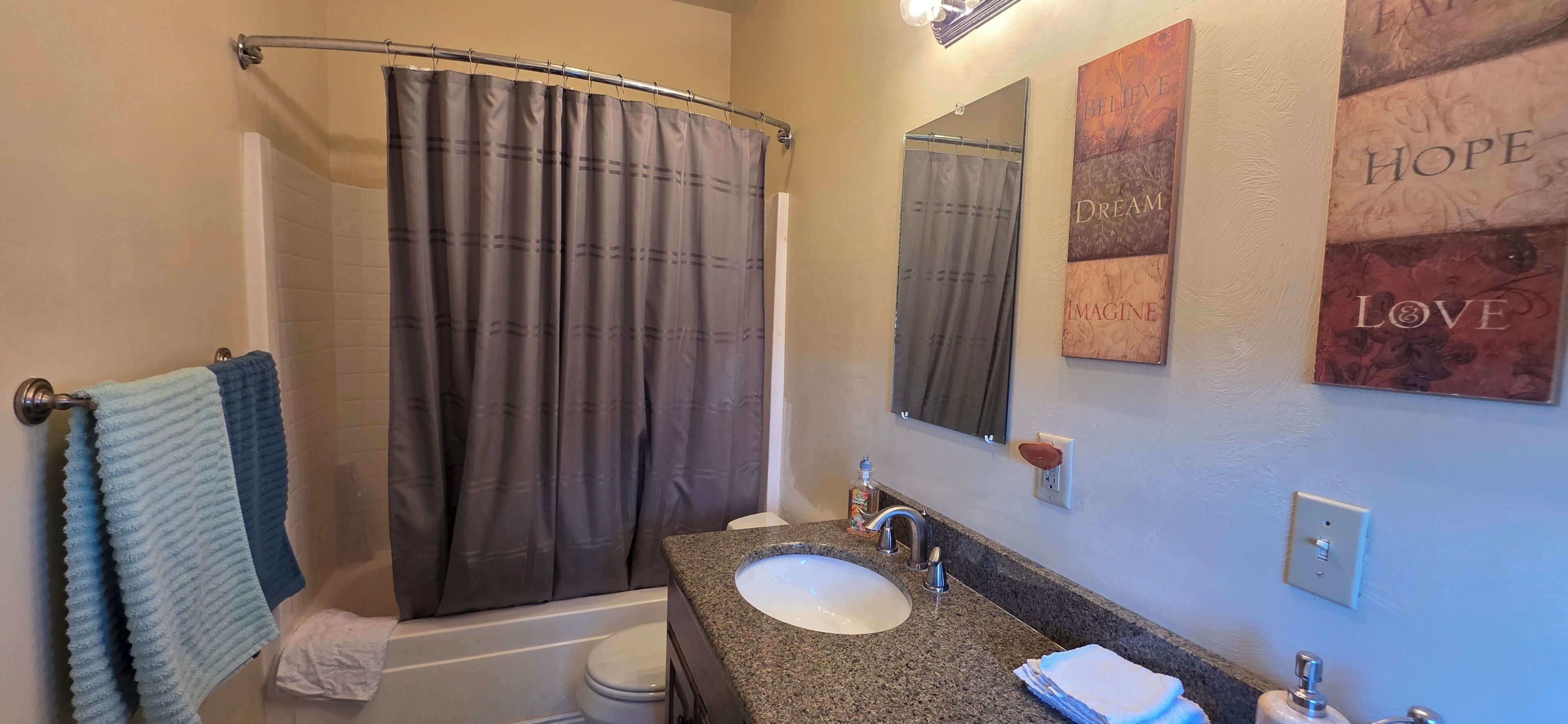 A bathroom with a shower curtain, a sink, a mirror, and a towel rack.