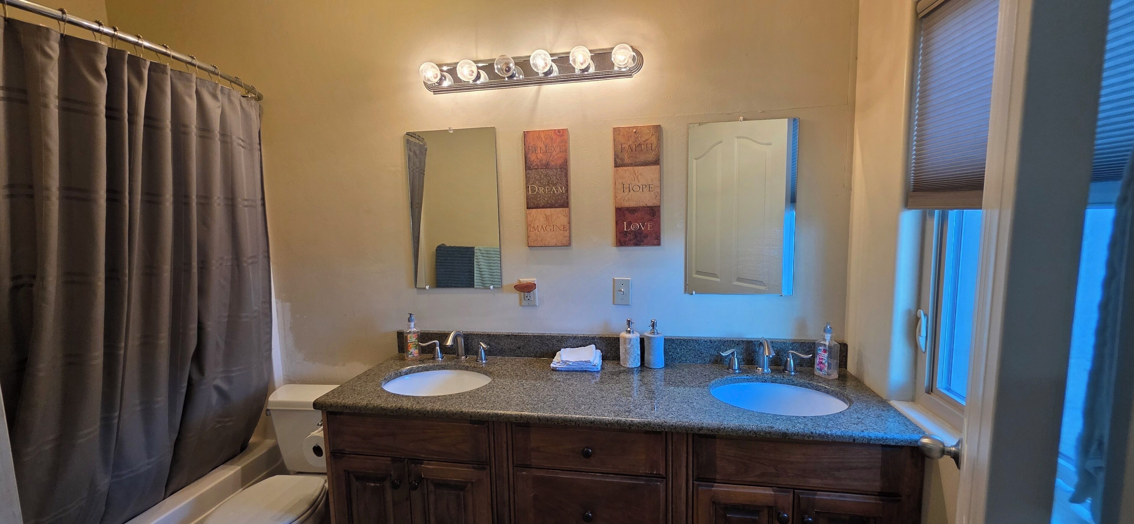Un bagno con due lavandini, una tenda della doccia, un mobile contenitore con cassetti, uno specchio e luci a parete.