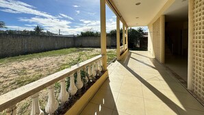 A covered outdoor area with a tiled floor, a concrete wall, and a metal railing. - Recanto Renascer (Aquiraz)
