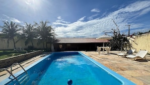 A rectangular swimming pool with a ladder on one side, surrounded by a patio area with lounge chairs and a table. - Recanto Renascer (Aquiraz)