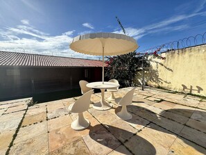 Un patio con una mesa, sillas y un gran paraguas, además de un piso de baldosas.