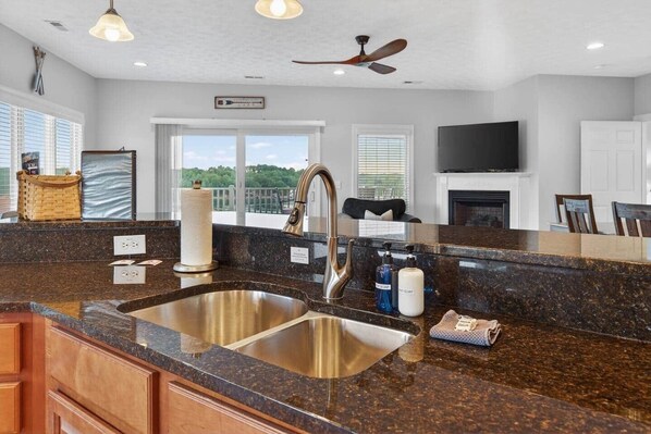 A modern kitchen with granite countertops, stainless steel sink, and a ceiling fan.