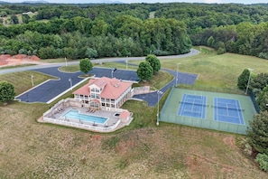 Une grande maison avec une piscine, des courts de tennis et une allée.