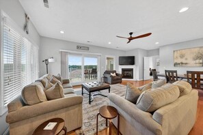 A spacious living room with a fireplace, a ceiling fan, and a balcony with outdoor furniture.