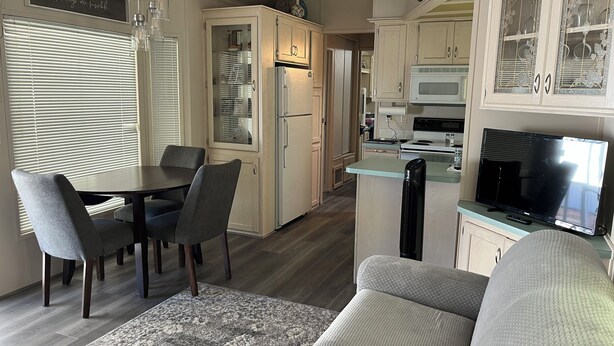 Cocina compacta con refrigerador, microondas y estufa, comedor con sillas y mesa, y sala de estar con sofá y televisor.