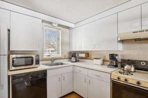 A compact kitchen with white cabinets, a microwave, a coffee maker, a kettle, and a stove. - Timeshare Unit in Prestigious Stowe, VT (Stowe)