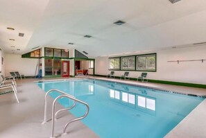 An indoor swimming pool with clear water, surrounded by lounge chairs and a small seating area. - Timeshare Unit in Prestigious Stowe, VT (Stowe)