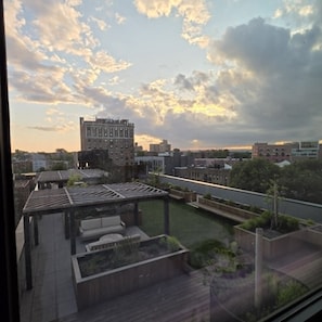 Ein Dachgarten mit einer Pergola, Blick auf eine Stadtlandschaft mit Gebäuden und einem bewölkten Himmel.