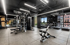 Ein Fitnessstudio mit unterschiedlichen Trainingsgeräten, großen Fenstern und Blick auf Gebäude.