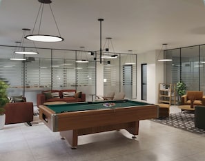 Ein moderner Billardtisch im Innenbereich mit Deckenbeleuchtung, eine Couch und ein Bücherregal in einem geräumigen Zimmer mit großen Fenstern.