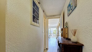 A hallway with textured walls, a wooden cabinet with a vase, and a door leading to an outdoor area. - California by Interhome (Le Grau du Roi)
