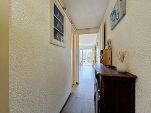 A hallway with textured walls, a wooden cabinet with a vase, and a door leading to an outdoor area. - California by Interhome (Le Grau du Roi)