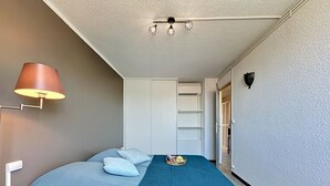 A bedroom with a bed, a lamp, a shelf, and a wardrobe. - California by Interhome (Le Grau du Roi)