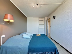 A bedroom with a bed, a lamp, a shelf, and a wardrobe. - California by Interhome (Le Grau du Roi)