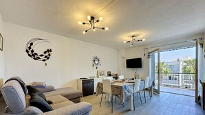 A modern living room with a sofa, dining table, chairs, a TV, and a balcony with a view. - California by Interhome (Le Grau du Roi)