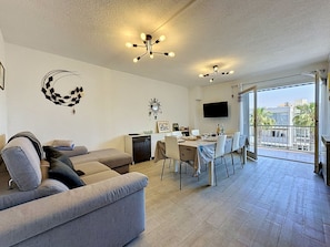 A modern living room with a sofa, dining table, chairs, a TV, and a balcony with a view. - California by Interhome (Le Grau du Roi)