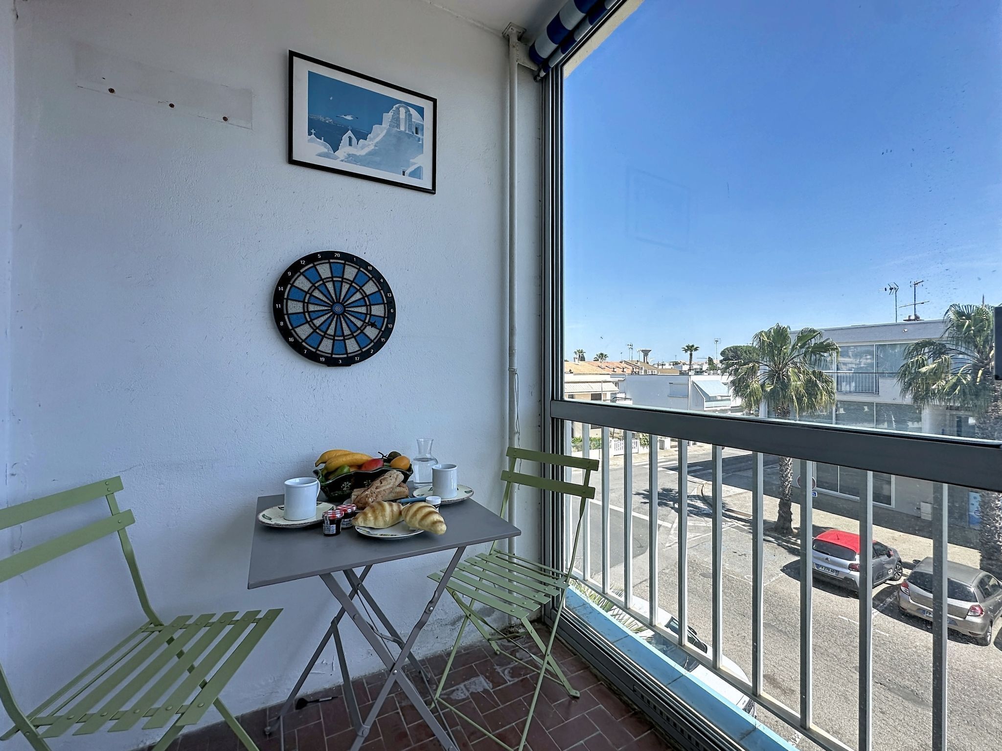 A balcony with a table, chairs, a dartboard, and a framed picture on the wall.
