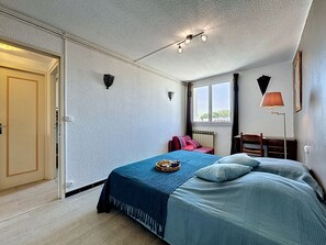 Een slaapkamer met een bed, nachtkastje, lamp, raam en een deur.