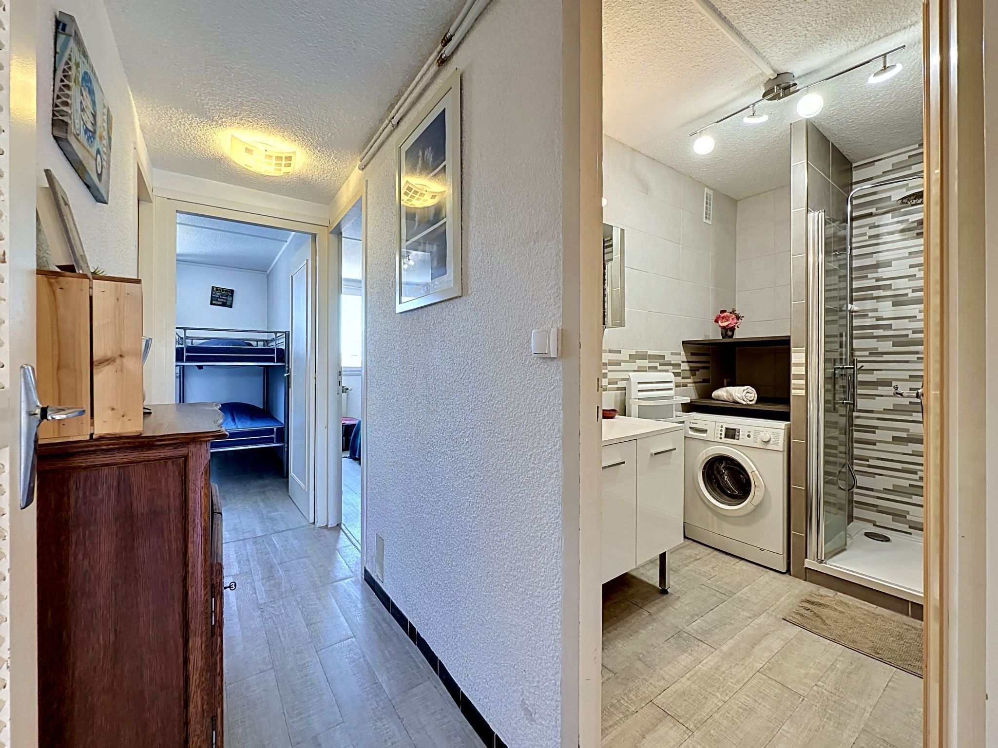 En korridor som leder till ett rum med våningssängar, en tvättmaskin och en dusch.