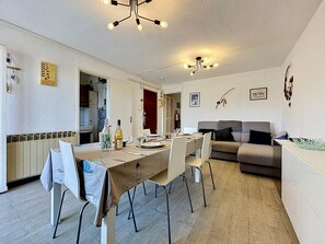 A dining area with a table set for four, a sofa, and a kitchen in the background. - California by Interhome (Le Grau du Roi)