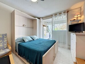 A bedroom with a bed, a TV, a wardrobe, and a window with curtains. - Les Floralies II by Interhome (Le Grau du Roi)