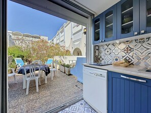 A compact kitchen with blue cabinets, a dishwasher, and a tiled backsplash. - Les Floralies II by Interhome (Le Grau du Roi)