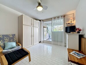 Ein Zimmer mit Deckenventilator, weißen Schränken, einer Holzbank, einem Fernseher und einem Fenster mit Vorhängen.